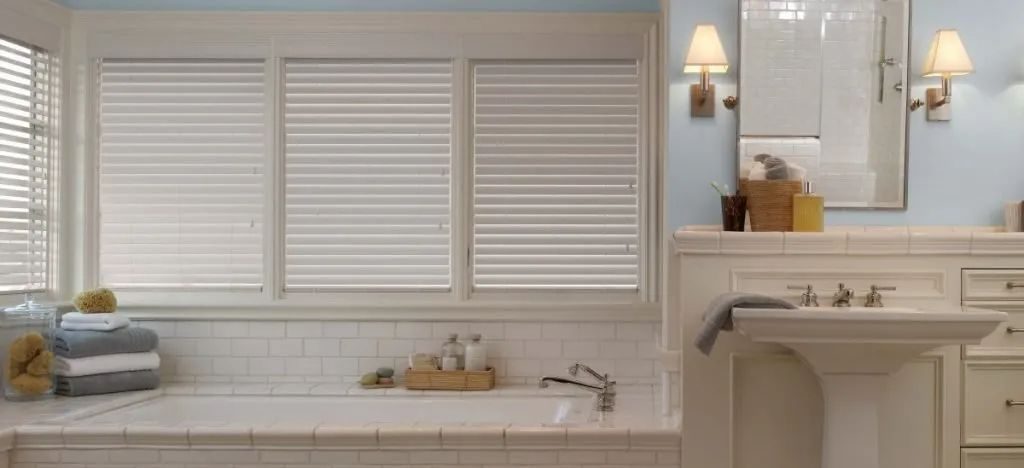 A bathroom with a tub , sink , mirror and eco-friendly blinds. Love is Blinds