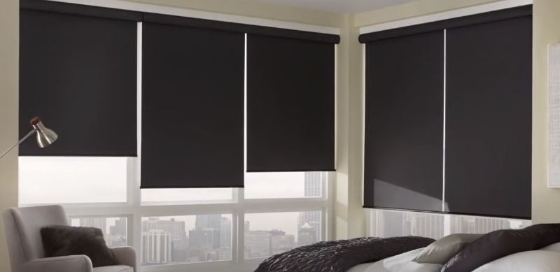 A bedroom in a high-rise has a corner of windows with navy roller shades.