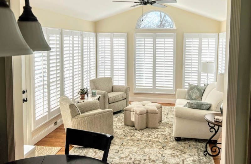A living room full of windows has white shutters and an arched window.
