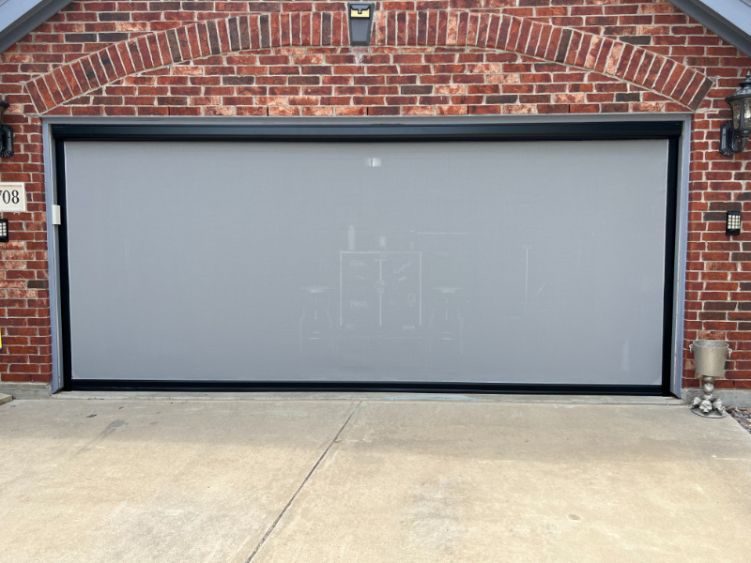 A red brick home has a garage with white exterior patio shades.