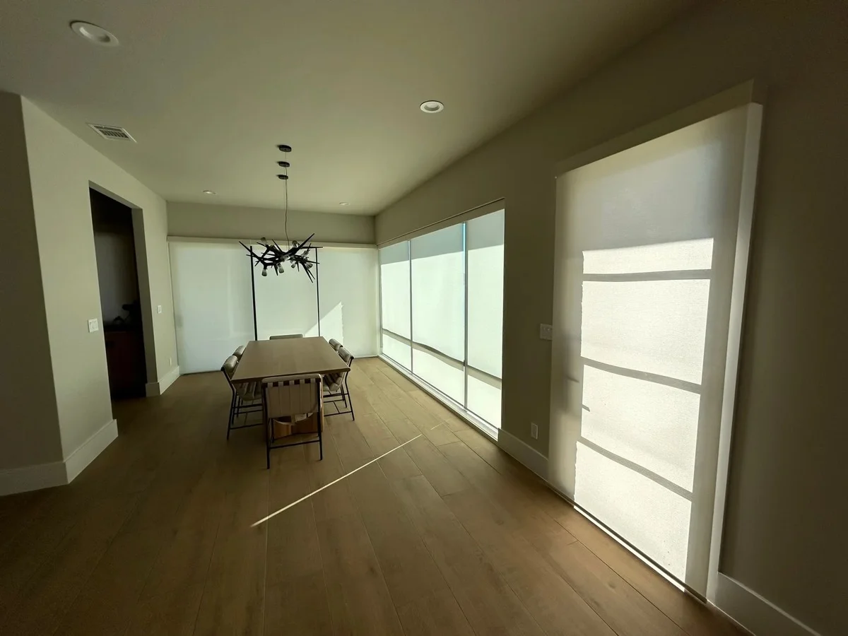 Roller shades lowered across tall windows in a modern Texas dining room