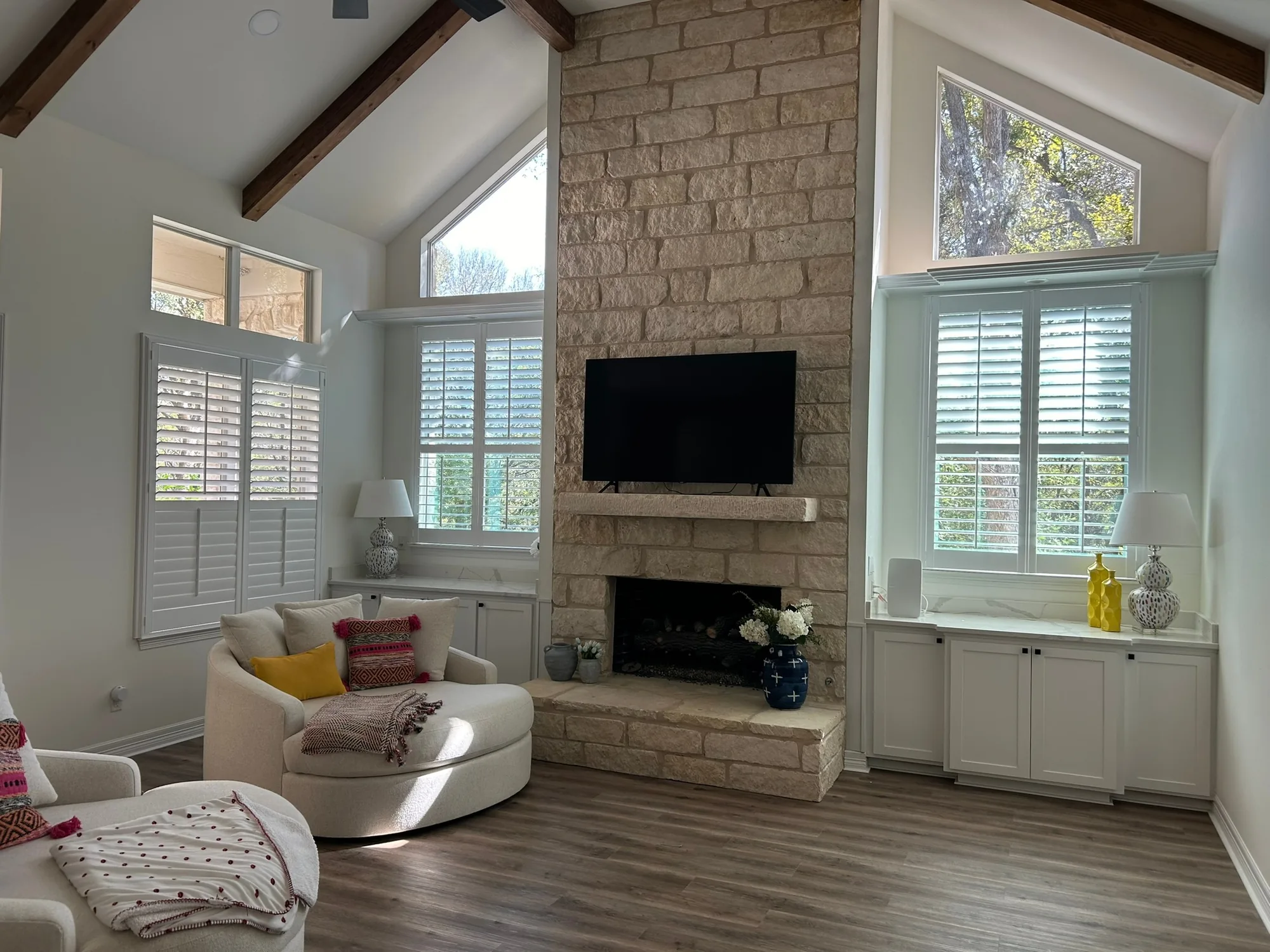 Plantation shutters in a vaulted Texas living room with a stone fireplace, installed by Love Is Blinds